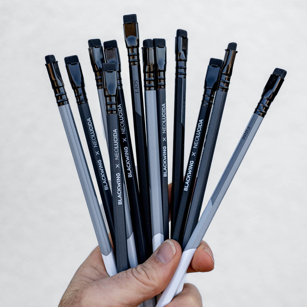 Hand holding a bundle of Blackwing Neolucida pencils with black and gray barrels