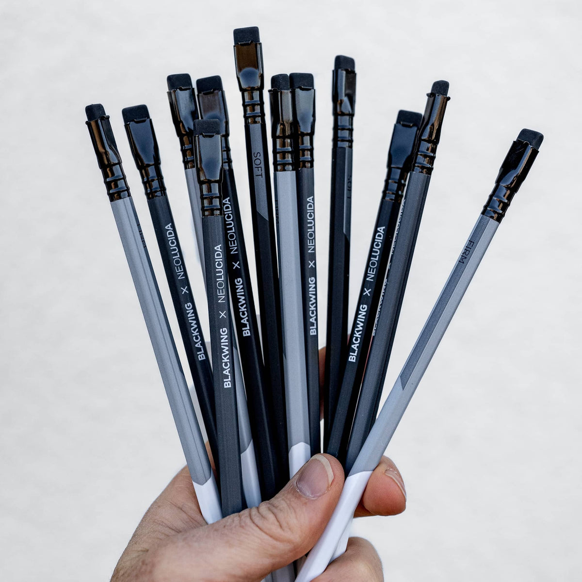 Hand holding a bundle of Blackwing Neolucida pencils with black and gray barrels