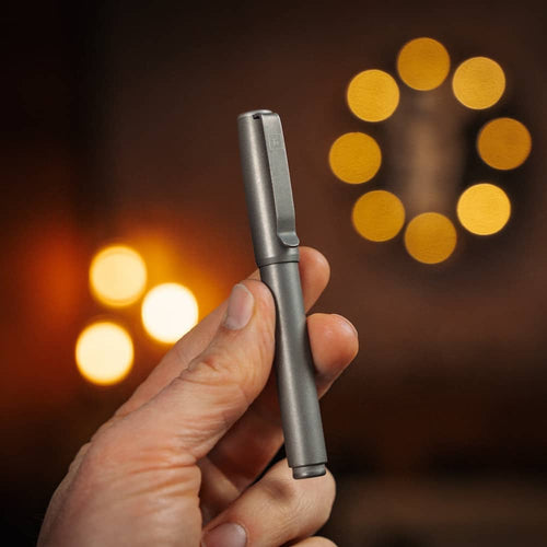 Hand holding a sleek titanium capped pen from BIG IDEA DESIGN LLC with blurred warm lights background
