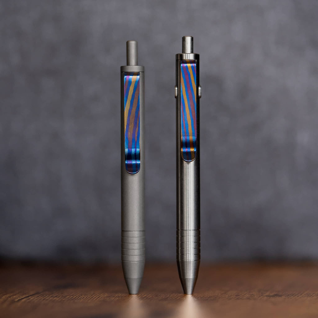 Two Big Idea Design LLC pens featuring titanium Damascus pen clip with blue and orange pattern